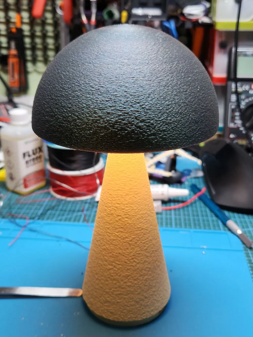 A mushroom-shaped printed lamp glowing warm on a workbench