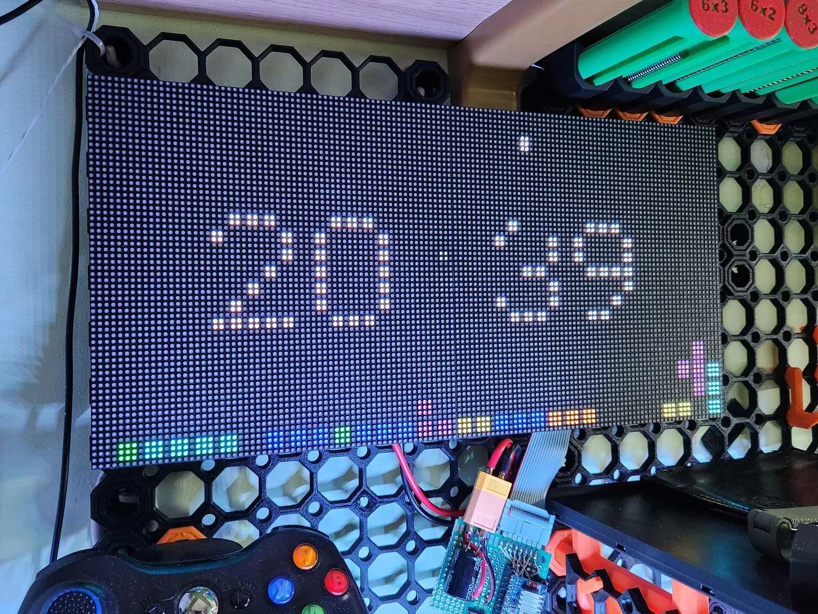 A 128x64 RGB LED matrix on a shelf showing the time with Tetris blocks stacking along the bottom