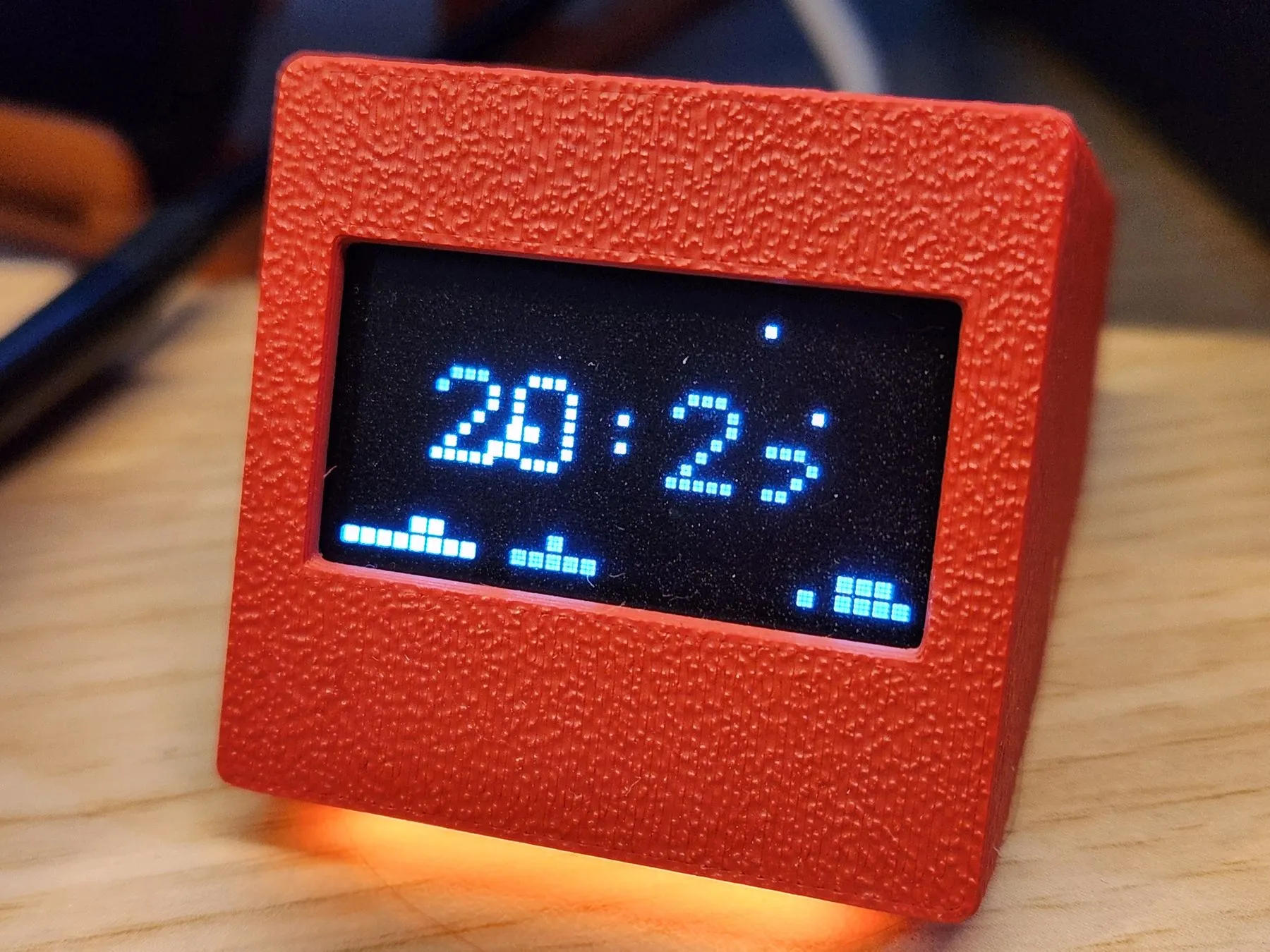 SmallOLED in a red printed case showing the animated clock face, warm light spilling underneath